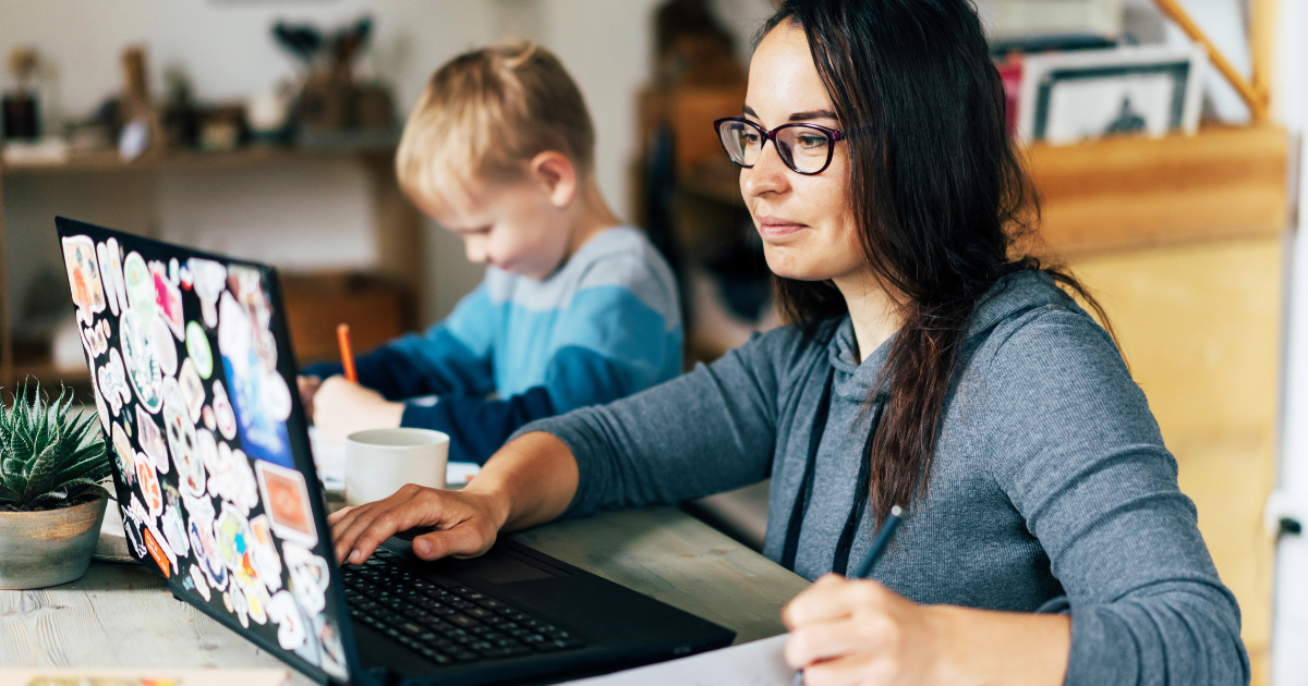 BetweenDeadlines&BedTimes_BlogImage Mom working at home on sticker-covered laptop with young boy next to her.